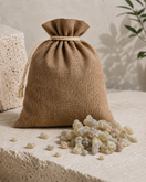 A small natural burlap drawstring pouch sits on a textured stone surface with Hojari Boswellia Sacra spilled in front of it. This shows 1KG size of premium resin. 