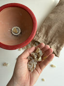 A hand holding small translucent resin next to an open red ceramic bowl and a brown burlap sack on a white surface.
