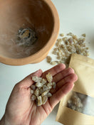 A hand holding a handful of natural Premium Hojari frankincense resin, with additional resin and a traditional resin burner softly visible in the background.