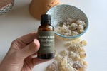 Person holding a bottle of Premium Omani Hojari Frankincense Essential Oil with authentic Boswellia sacra frankincense resin displayed in the background, sourced from Dhofar, Oman.